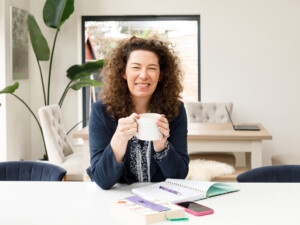 Woman with brown curly hair, smiling whilst holding a mug. Sophie Comas.